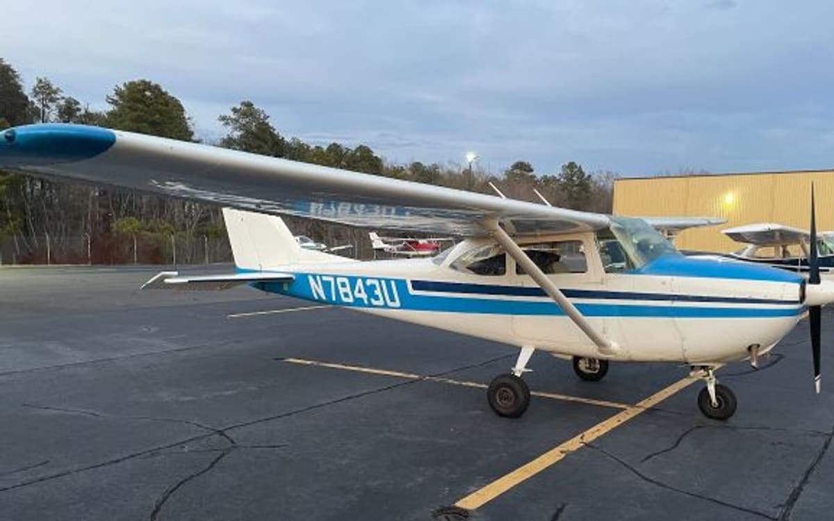 A blue-and-white Cessna 172 Skyhawk registered N7843U parked on the ramp at last light, with a lit hangar behind it.