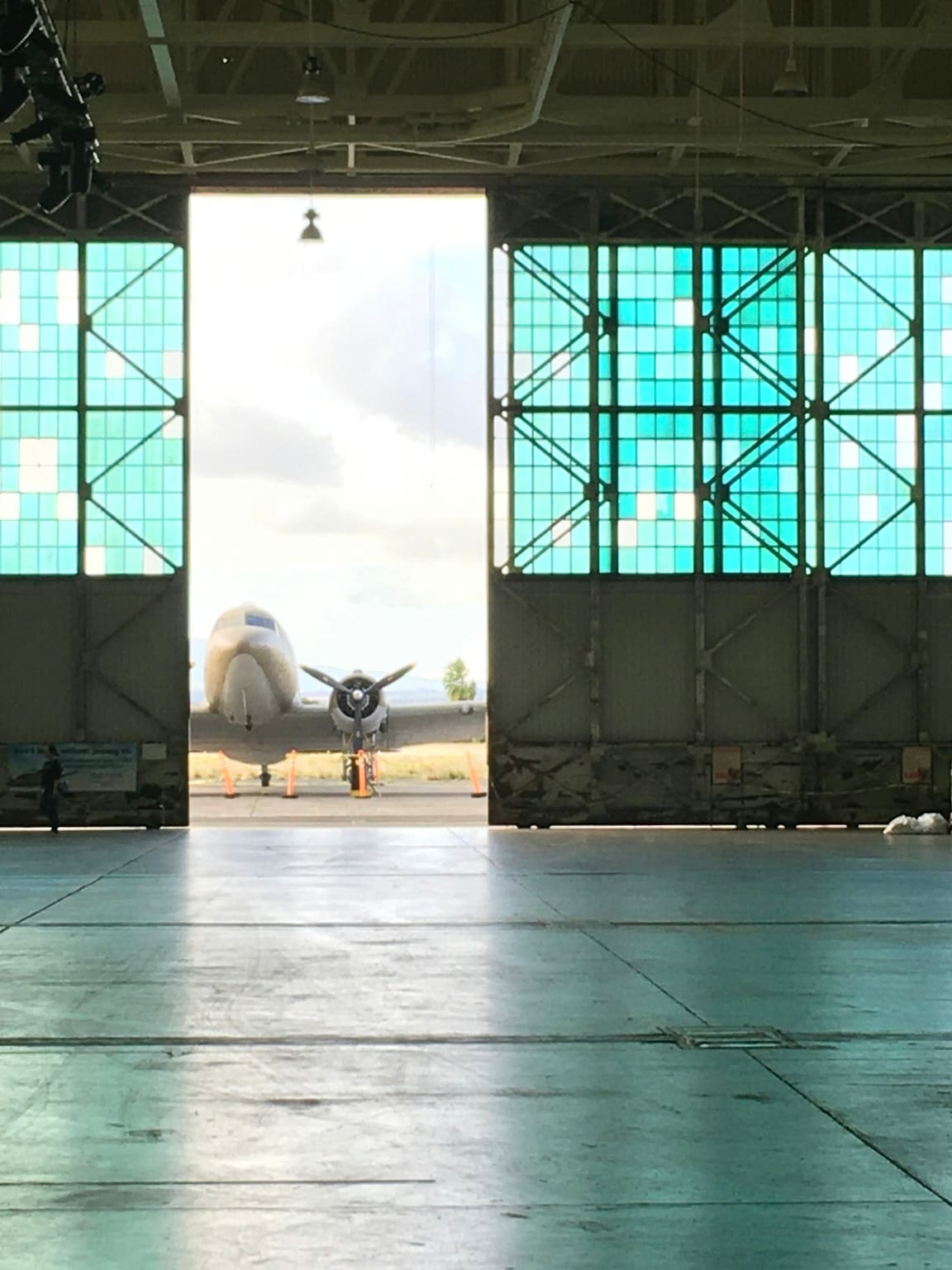 The inside of a hangar looking out through its open door to an aeroplane parked on the apron in daylight.